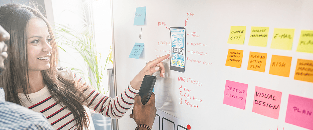 two adults pointing to post its on a white board