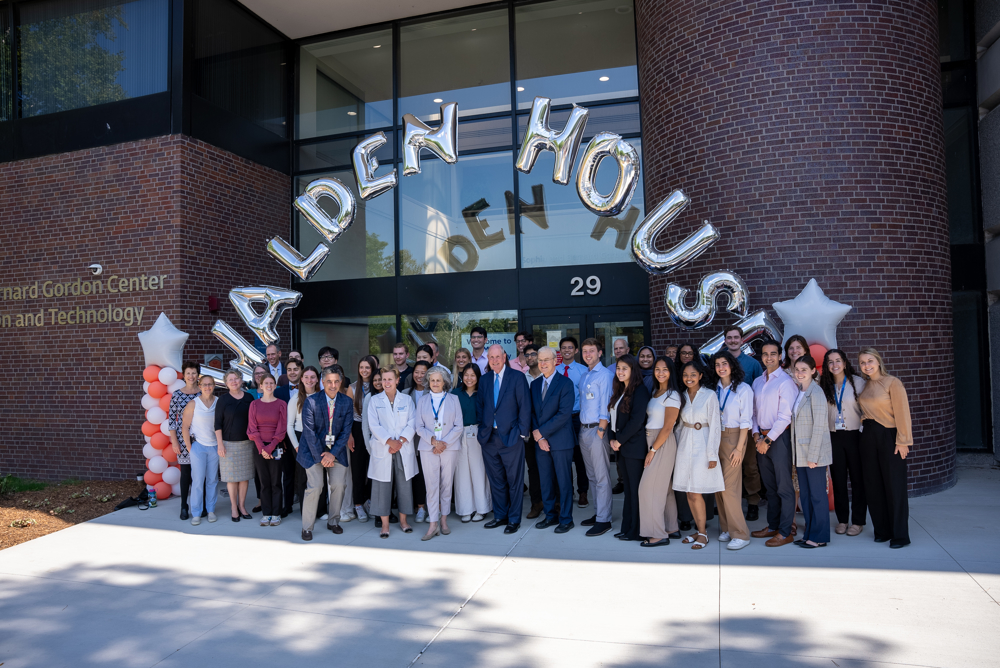 The inaugural cohort of LEAD@Lahey medical students—32 strong—gather on the UMass Chan-Lahey regional campus in Burlington. They are gathered in front of a building below a balloon arch thats spells out Walden House.