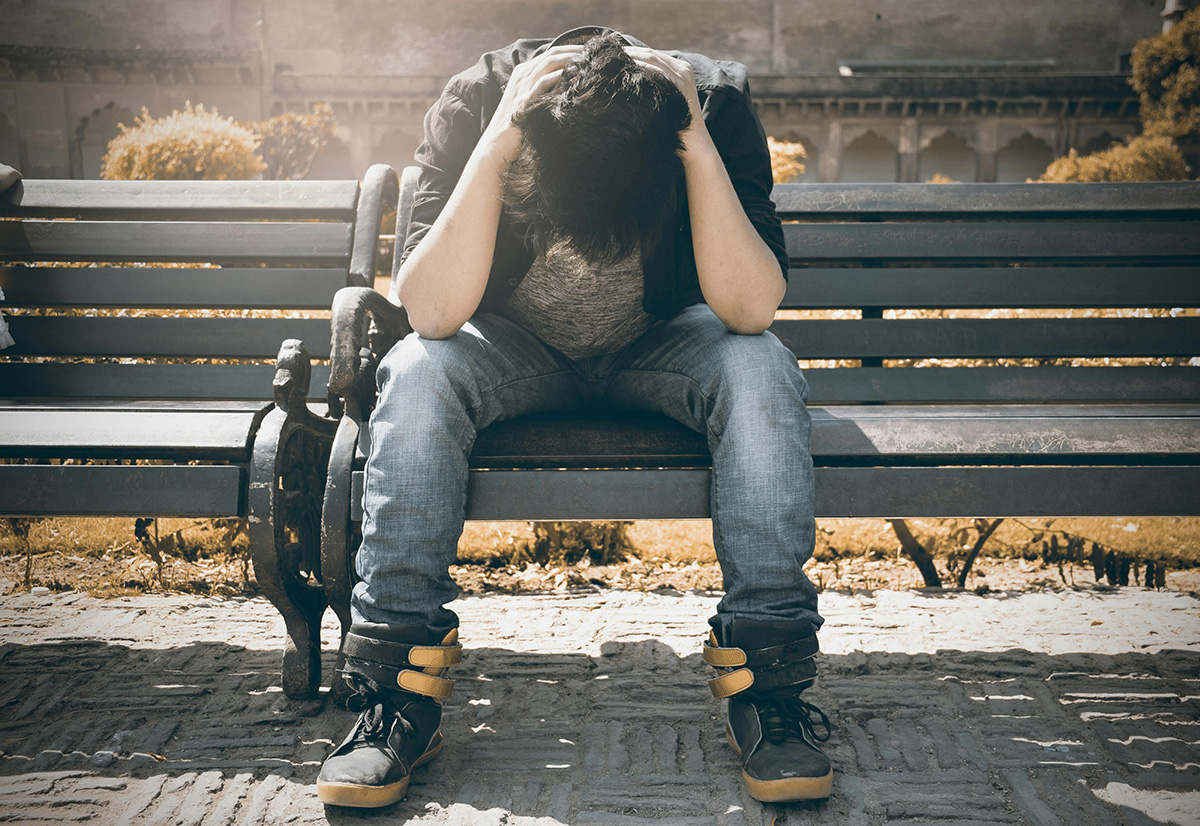 man sitting on a park bench bent over with head in hands