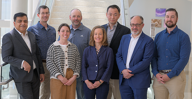 Group shot of Parth Chakrabarti, Scot Wolfe, Lauren Zingarelli, Paul Thompson, Sharon Cantor, Li Li, George Xixis, and Andrew Moomey in front of a staircase