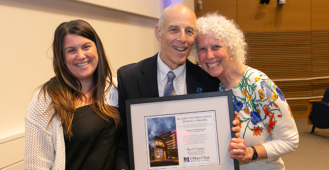 Arnold S. Freedman, Hannah Freedman and Lori Kahn standing together with framed Alumni Distinguished Service Award